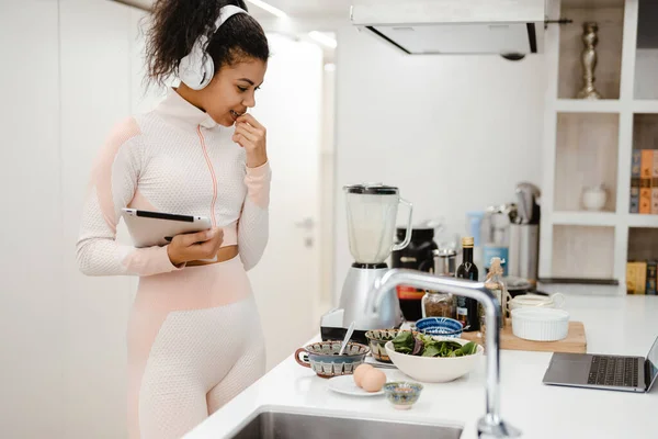 Musta Nainen Kuulokkeissa Käyttäen Tablet Tietokonetta Ruoanlaitossa Kotona — kuvapankkivalokuva