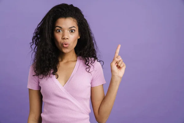 年轻的黑人妇女指尖向上 同时在紫色背景下表现出惊讶的表情 — 图库照片