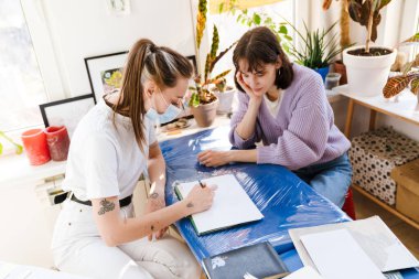 Genç beyaz kadınlar atölyede çalışırken eskizler çiziyorlar.