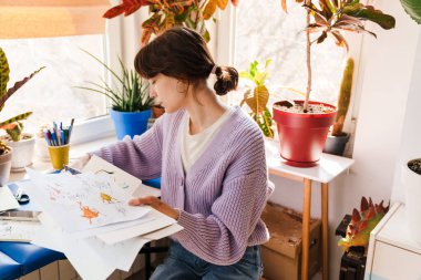 Genç beyaz kadın evde otururken eskizlerle çalışıyor.