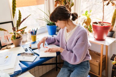 Genç beyaz kadın evde otururken eskizlerle çalışıyor.