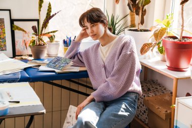 Evde otururken eskiz defteriyle çalışan genç beyaz kadın.