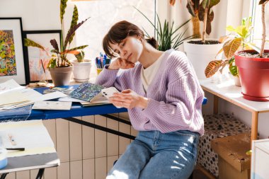 Genç beyaz kadın evde otururken cep telefonu kullanıyor.