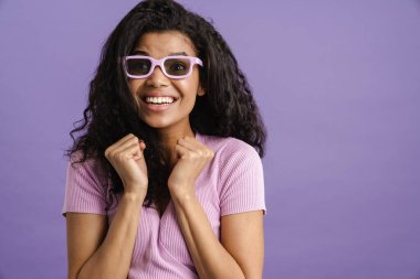 Güneş gözlüklü genç siyahi kadın mor arka planda izole edilmiş kameraya bakıyor.