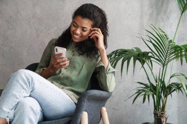 Siyah genç bir kadın koltukta otururken cep telefonu kullanıyor.