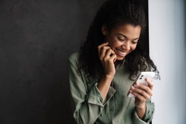 Kapalı alanda cep telefonu kullanırken gülen genç siyahi kadın.