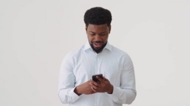 Beyaz stüdyoda telefonla mesaj atan gülümseyen Afrikalı adam.