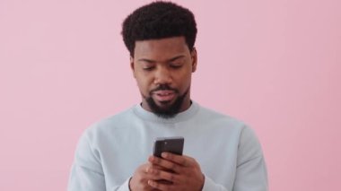 Mutlu Afrikalı adam telefonla mesaj atıyor ve pembe stüdyoda konuşuyor.