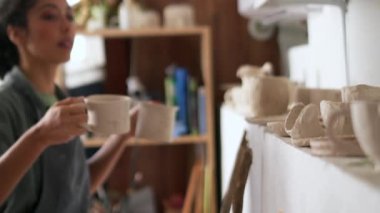 Kadın çömlekçi atölyeye kilden bardak koyar.