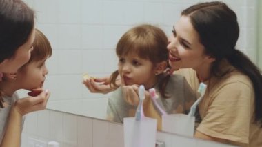 Güzel anne banyoda kızının dudaklarına dudak kremi sürüyor.