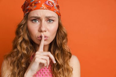 Bandana takan genç kızıl kadın turuncu duvarda izole edilmiş sessizlik hareketi gösteriyor.