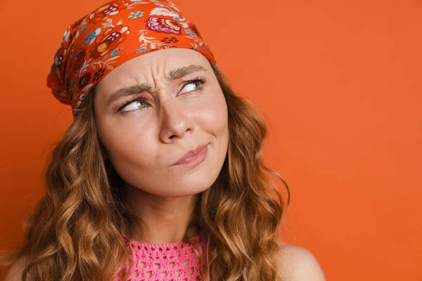 Bandana takan genç kızıl saçlı kadın turuncu duvarın üstünde soyutlanmış ve yukarı bakıyor.