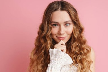 Kızıl elbiseli genç kadın gülümsüyor ve pembe duvarın üzerinden izole edilmiş kameraya bakıyor.