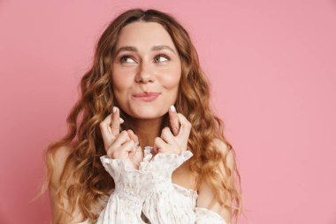 Şans dilerken gülümseyen kızıl saçlı genç bir kadın pembe duvarın üzerinde kapalı bir şekilde şans diliyor.