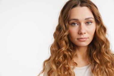 Tişört giyen genç kızıl kadın beyaz duvarın üzerinden izole edilmiş kameraya bakıyor.