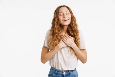 Beyaz duvarın üzerinden izole edilmiş, gülümseyen ve göğsünde el ele tutuşan kızıl saçlı genç kadın.