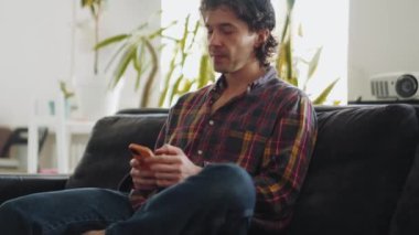Ekose gömlekli konsantre yetişkin bir adam telefonla mesaj atıyor ve evde konuşuyor.