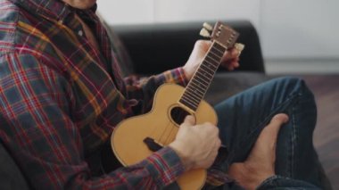 Ekose gömlekli adam evde ukulele çalıyor.