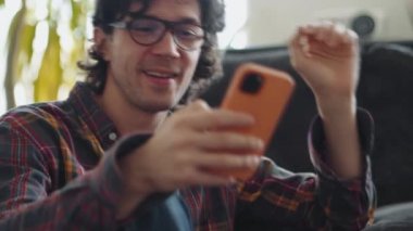 Ekose gömlekli gülen yetişkin adam evde telefonla mesaj atıyor.