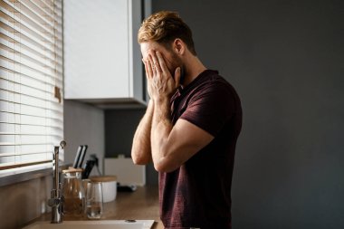 Çekici bir genç adam mutfak lavabosunun önünde dikilirken pencereden bakıyor.
