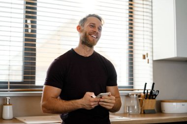 Mutfakta cep telefonu kullanan yakışıklı genç adam.