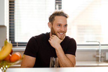 Sağlıklı bir adam mutfakta dururken bardaktan su içerek gülümsüyor.