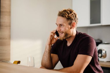 Mutfakta cep telefonu kullanan yakışıklı genç adam.