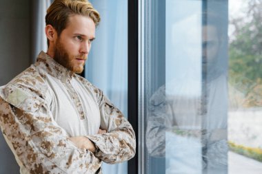 Erkek, kendine güveni tam bir asker ayakta ve pencereden dışarı bakıyor.