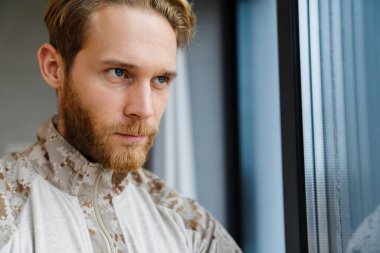 Erkek, kendine güveni tam bir asker ayakta ve pencereden dışarı bakıyor.
