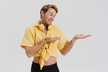 Kulaklıklı, gülümseyen ve kopyalama alanı tutan kızıl saçlı genç adam beyaz duvarın üzerinde izole edilmiş.