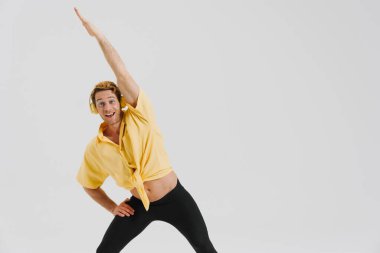 Beyaz duvarın üzerinde izole edilmiş egzersiz yaparken kulaklıklı genç adam gülümsüyor.