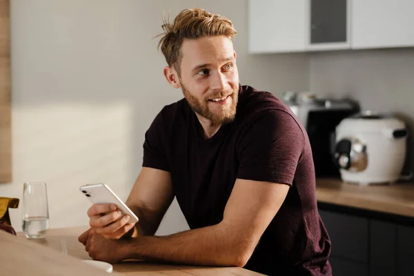 Fešák Mladý Muž Pomocí Mobilního Telefonu Kuchyni — Stock fotografie