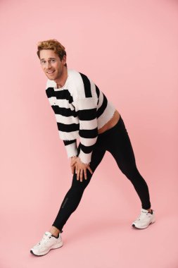 Tayt giyen genç adam pembe duvarda tek başına egzersiz yaparken gülümsüyor.