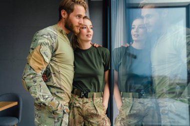 Güzel, genç, asker bir çift kucaklaşıp pencereden dışarı bakıyor.