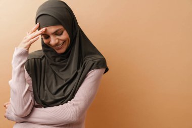 Türbanlı genç Müslüman kadın bej arka planda izole edilmiş kameraya gülüyor.