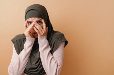 Başörtülü genç Müslüman kadın bej arka planda izole edilmiş.