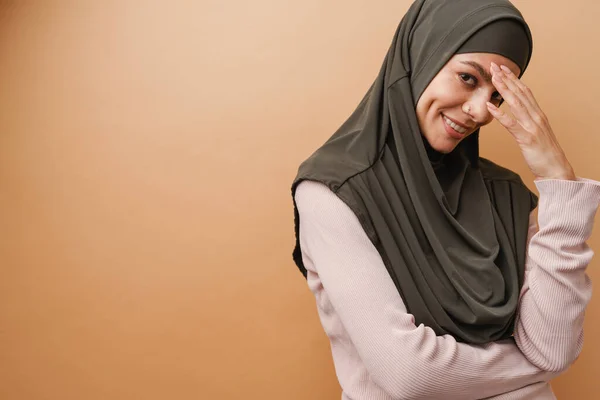 头戴头巾的年轻的穆斯林妇女嘲笑被米色背景隔离的相机 — 图库照片