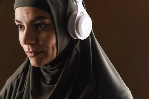 Молодая Мусульманка Хиджабе Слушает Музыку Наушниками Коричневом Фоне — стоковое фото