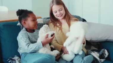 Mutlu çok uluslu kardeşler evdeki kanepede konuşuyor ve oyuncaklarla oynuyor.