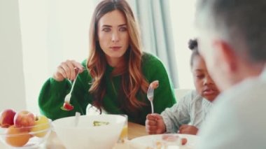 Çok uluslu ciddi bir aile kahvaltısını yapıyor ve evde konuşuyor.