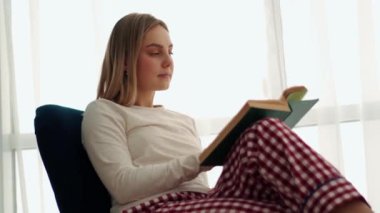 Evde kitap okuyan konsantre sarışın kadın.