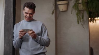 Kulaklık takan neşeli adam kafede telefonla bir şey izliyor.