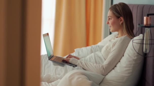 快乐的金发女人在家里的床上用笔记本电脑通过视频通话 — 图库视频影像