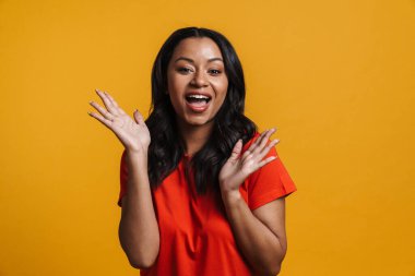 Mutlu orta yaşlı Afrikalı sıradan bir kadın sarı duvar arkasında duruyor, kutluyor, dans ediyor.