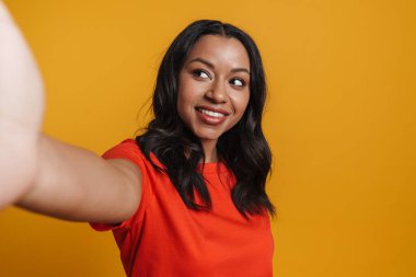 Sarı arka planda izole edilmiş selfie çekerken gülümseyen genç zenci kadın.