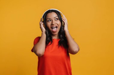 Sarı arka planda izole edilmiş kulaklıklarla müzik dinleyen siyahi genç bir kadın.