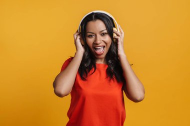 Sarı arka planda izole edilmiş kulaklıklarla müzik dinleyen siyahi genç bir kadın.