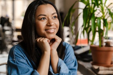 Kafede otururken gülümseyen ve yan bakan siyahi genç kadın.