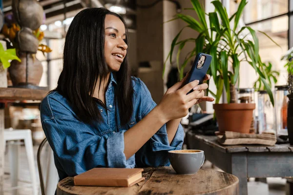 Negro Sonriente Mujer Usando Teléfono Celular Mientras Está Sentado Cafetería —  Fotos de Stock