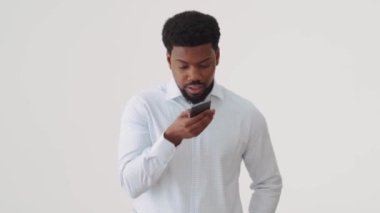 Ciddi bir Afrikalı, beyaz stüdyoda telefonla sesli mesaj kaydediyor.